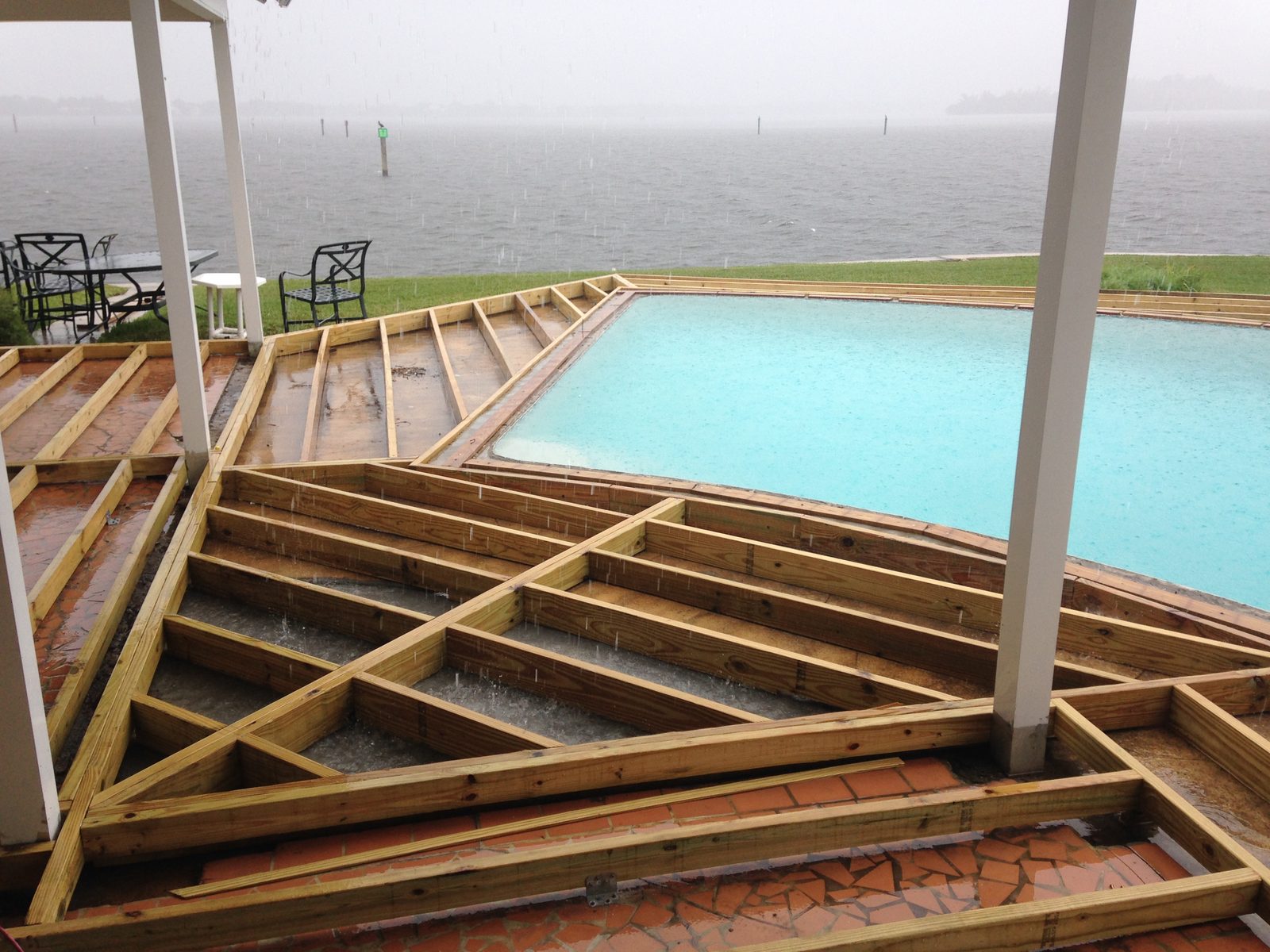 Pressure-treated deck framing wrapping a riverfront pool during a rain shower
