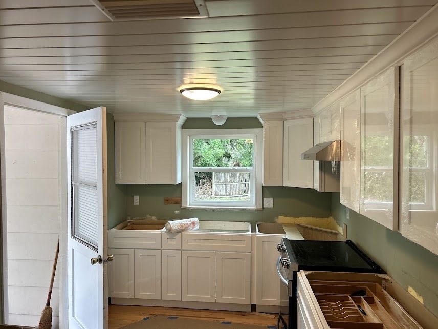 Remodeled kitchen with white shaker cabinets, green walls and a plank ceiling