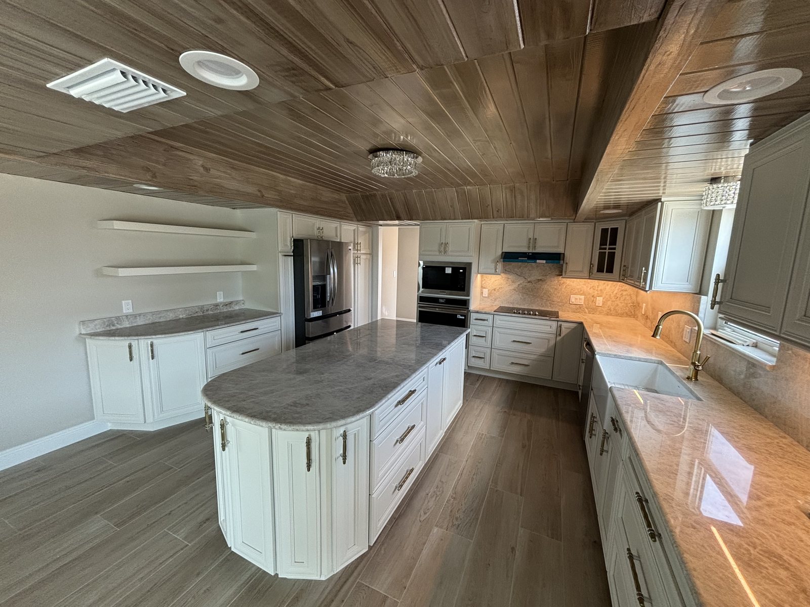 Remodeled kitchen with a marble top island, white raised panel cabinets and a wood plank ceiling