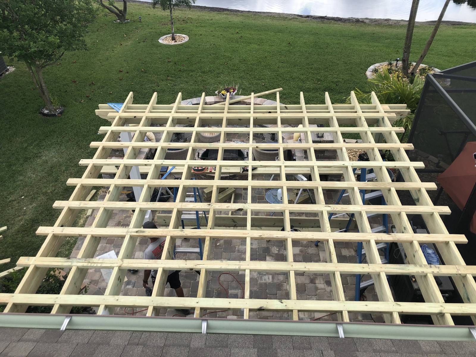 Pergola rafters being framed above a paver patio and fire pit