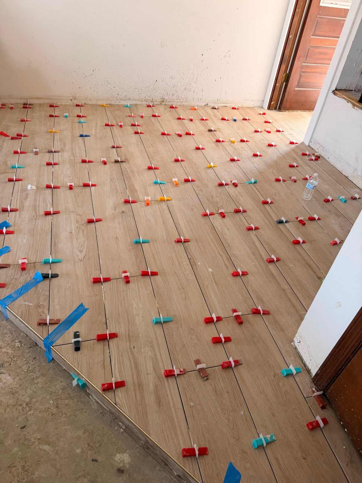 Wood-look tile plank floor set with leveling clips during installation