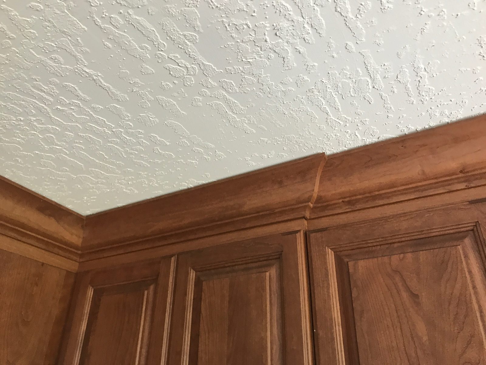 White crown molding scribed tight to the ceiling above cherry kitchen cabinets